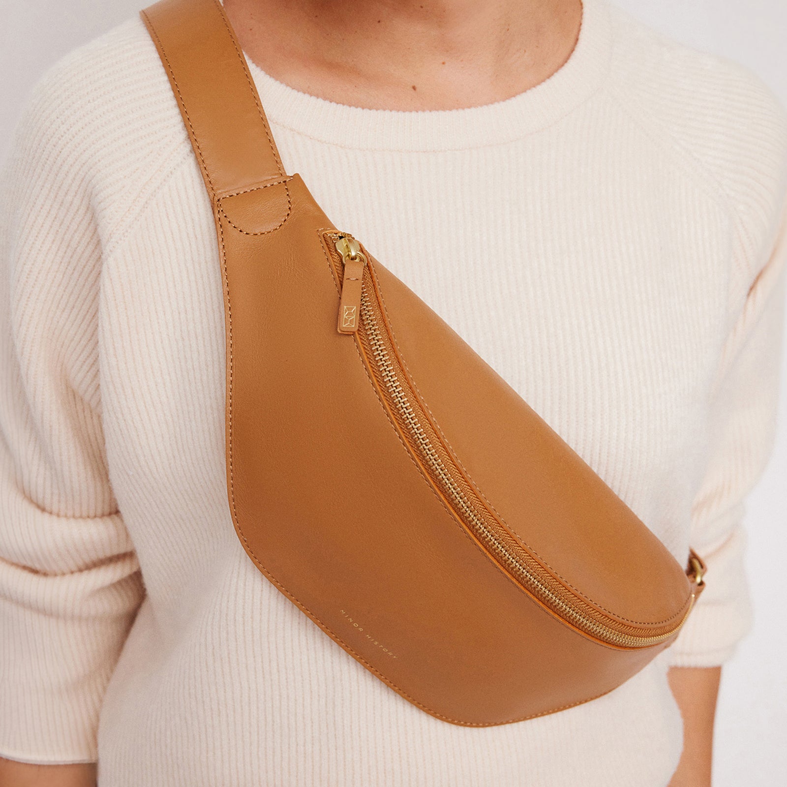 Crosstown belt bag in saddle brown full-grain leather, cropped detail highlighting leather texture and stitching