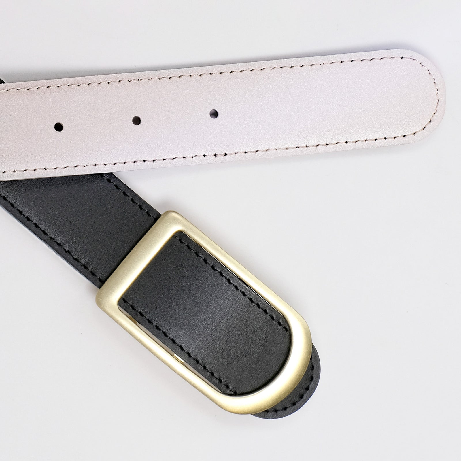 Gemini reversible belt in black and pearl full-grain leather with brass buckle, close-up of buckle and leather texture