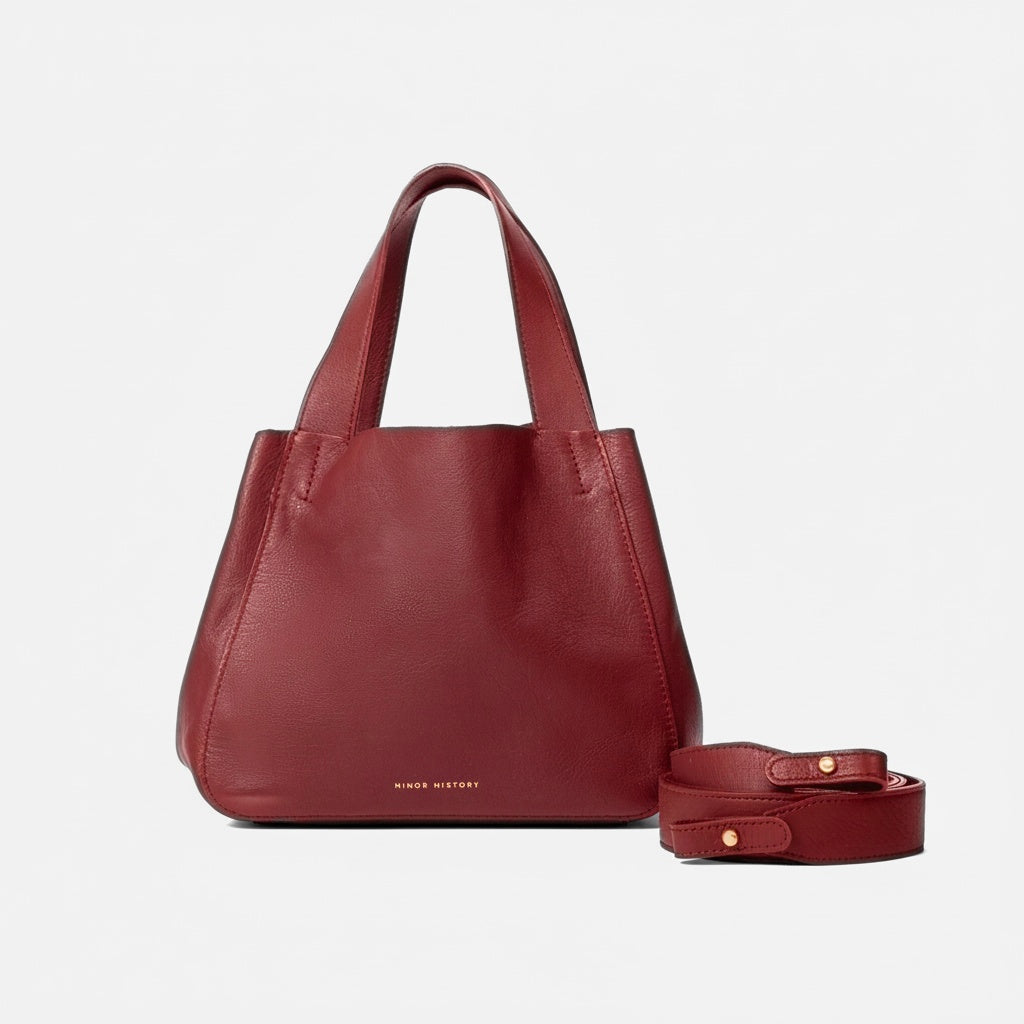 Red leather handbag with matching strap on a light gray background - Cherry Cola