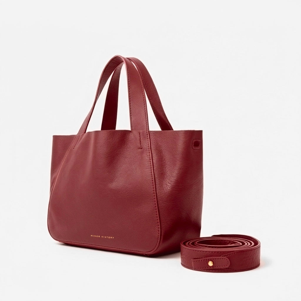 Black leather tote bag with matching strap on a light gray background - Cherry Cola