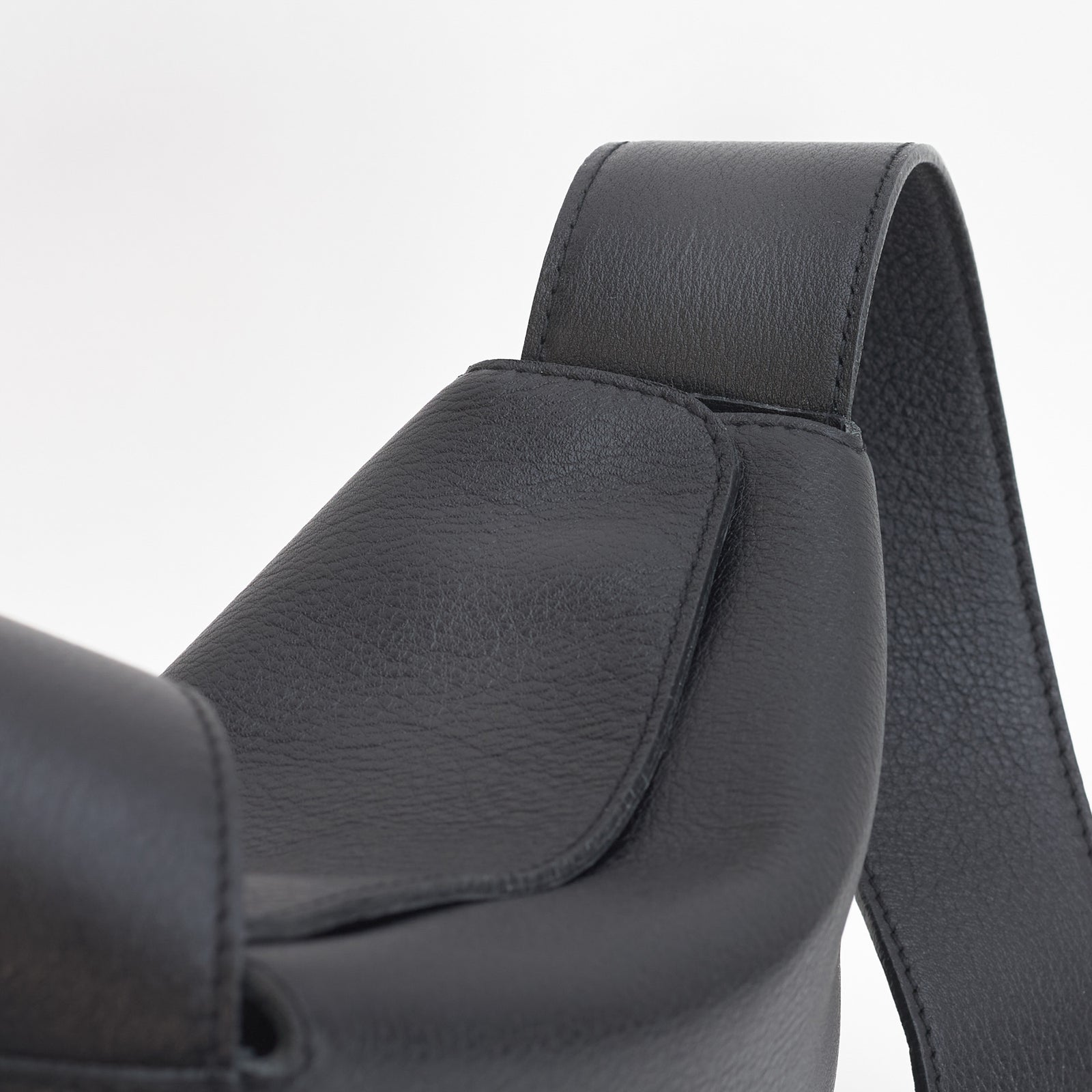 Little Frame crossbody bag in black full-grain leather, close-up of strap attachment and smooth texture, minimalist women's handbag