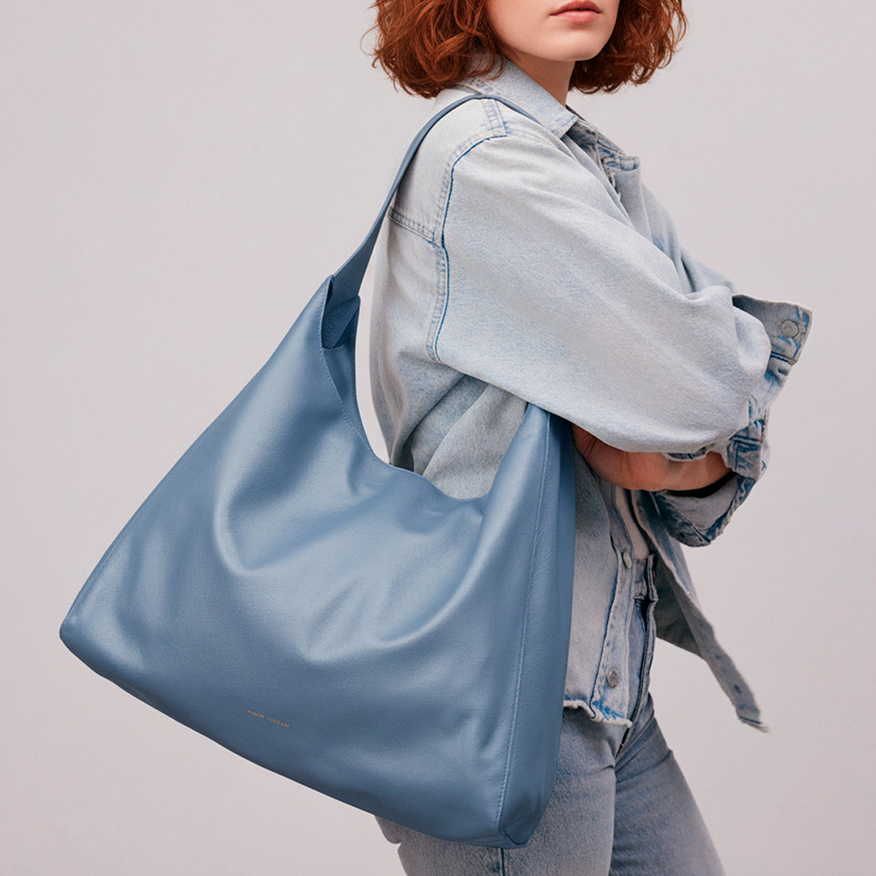 Person holding a blue bag against a plain background - Chambray