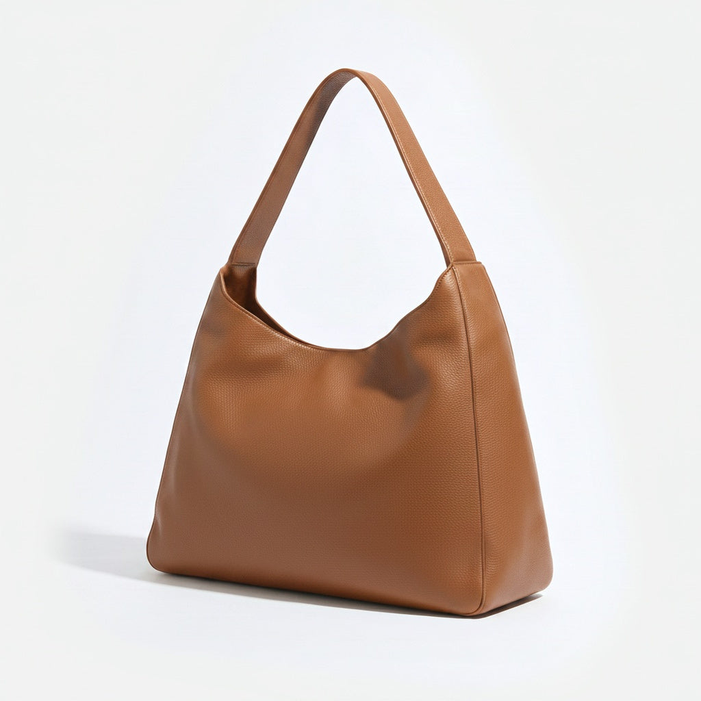 A medium brown pebbled leather hobo shoulder bag with a single strap, shown from a three-quarter angle on a clean white background. -Saddle