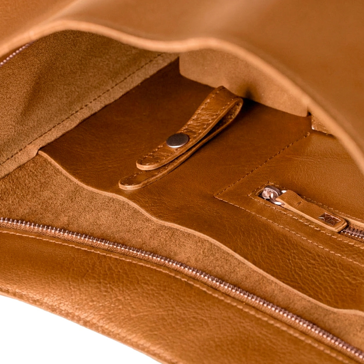 Close-up of a brown leather bag with zippers and stitching details. - Saddle