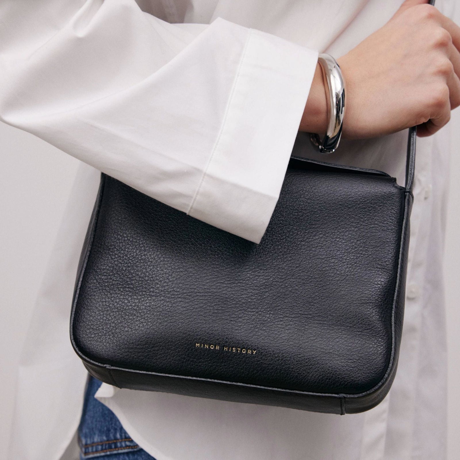 Little Frame crossbody bag in black full-grain leather carried by hand with tailored trousers for a polished style, minimalist women's handbag