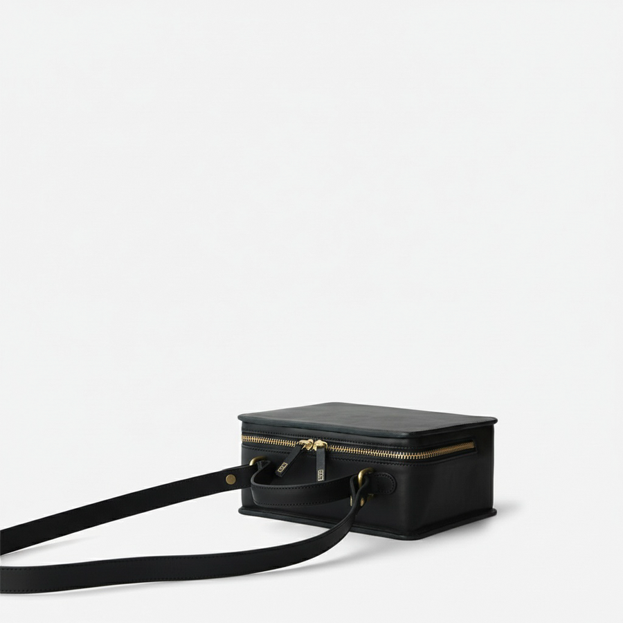 Black Box Top Handle Crossbody, laid on its back showing the zipper, strap attachments and long strap - Black