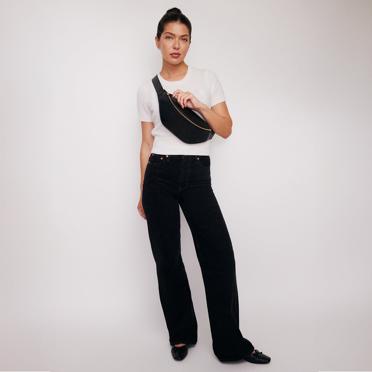 Crosstown sling bag in black full-grain leather, cropped detail highlighting leather texture and stitching