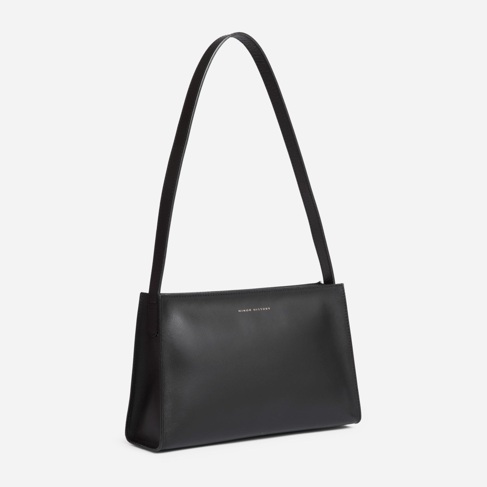 A brown leather shoulder bag with a minimal design, a sturdy zipper, and a delicate shoulder strap, displayed against a white background. - Saddle