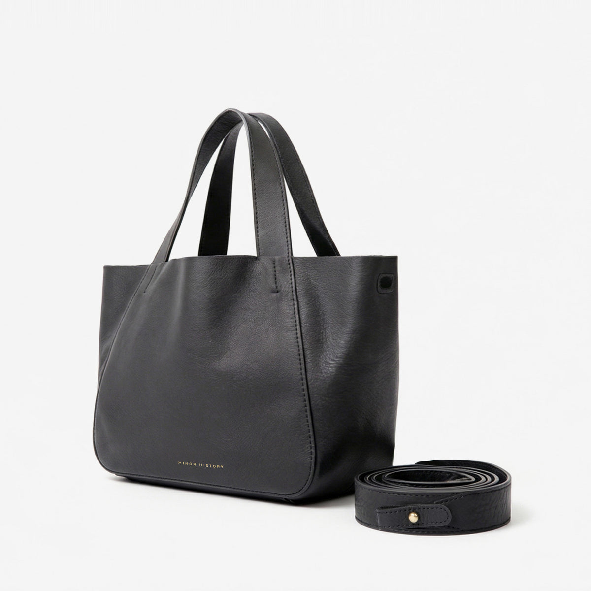 Black Little Times Tote, angled front view with the removable strap coiled beside it - Black