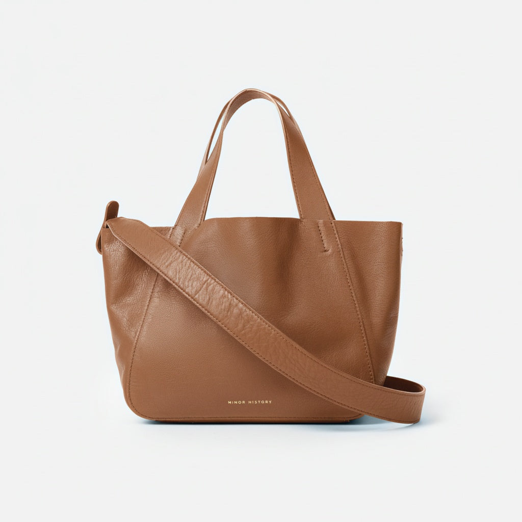 Brown leather tote bag with a shoulder strap on a light gray background - Saddle