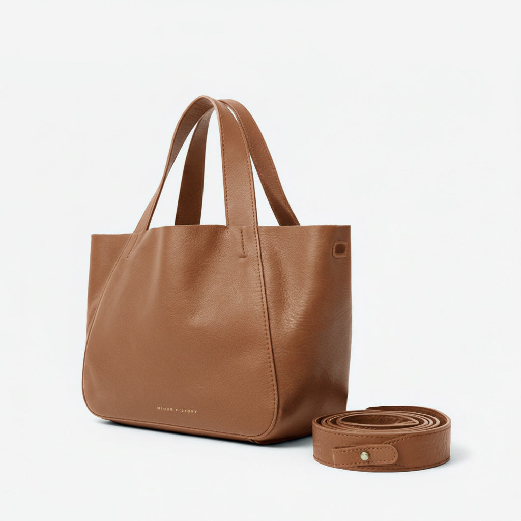 Brown leather tote bag with matching strap on a light gray background - Saddle