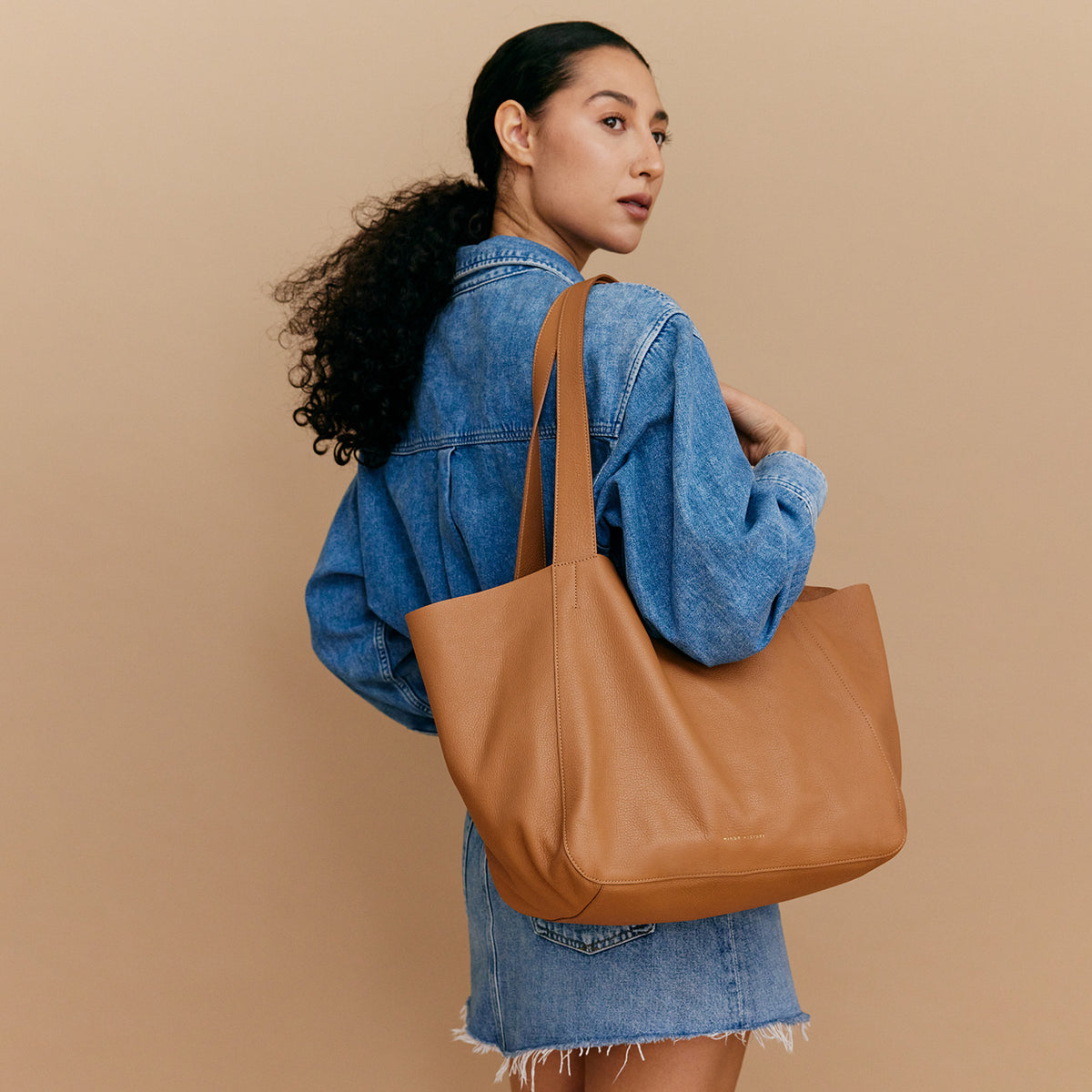 The Times Tote worn over the shoulder, showing both long handles and how the bag hangs at the side - Saddle