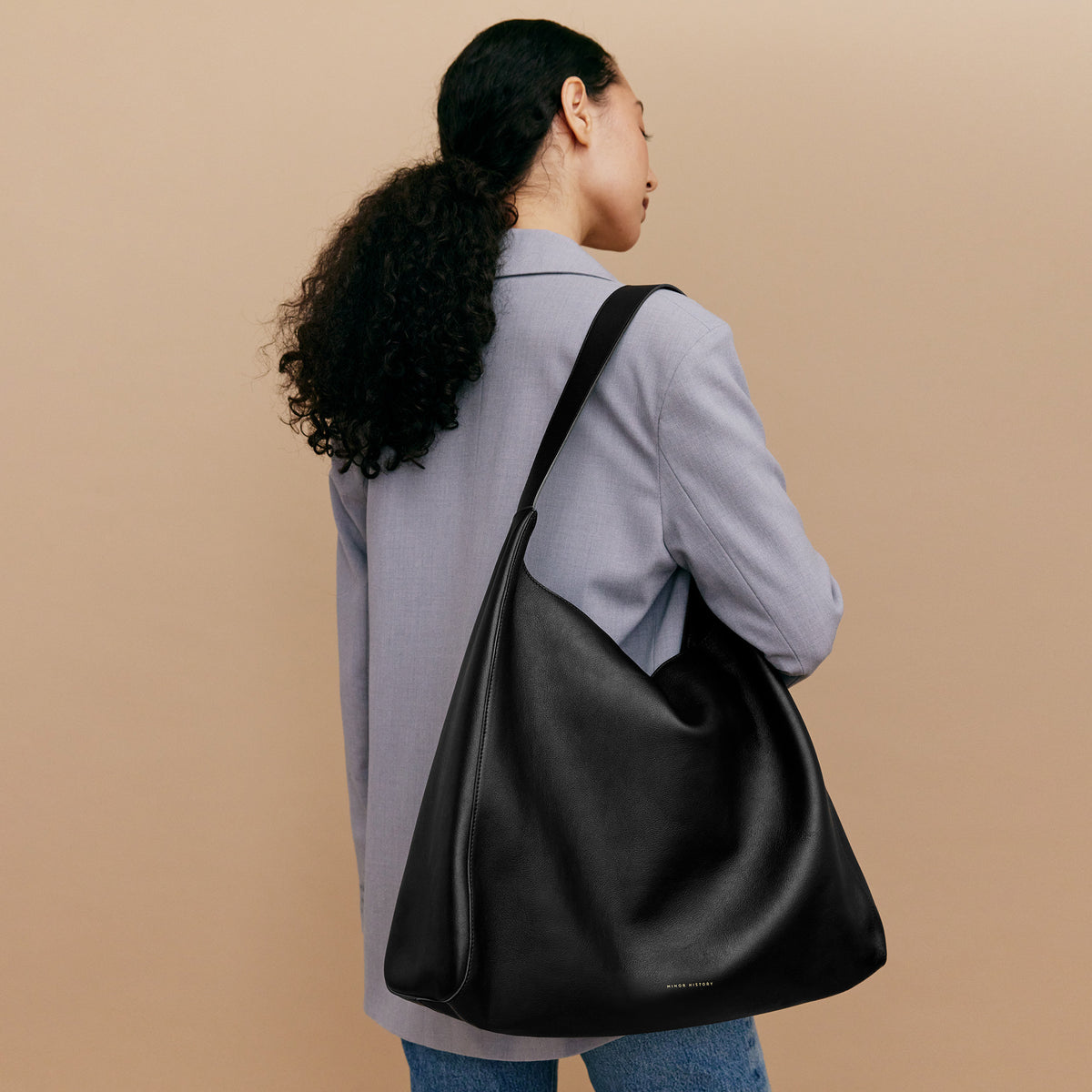 The Overtime Tote worn over the shoulder with a blazer, showing the long strap and generous bag body at the side - Black