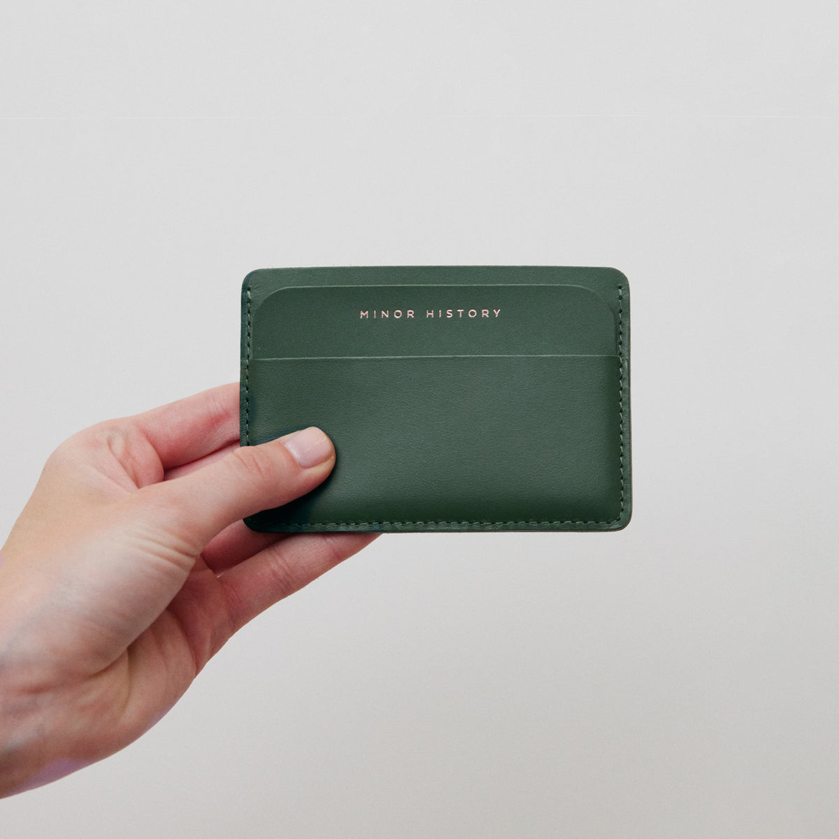 Hand model holding Midtown Evergreen leather wallet