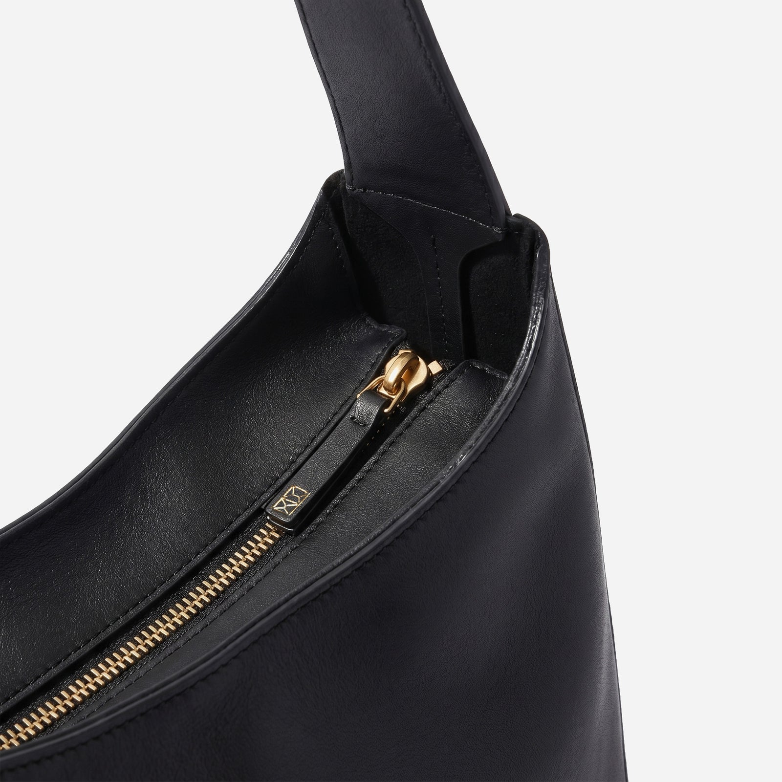 Black handbag with gold zipper on a light gray background -Black