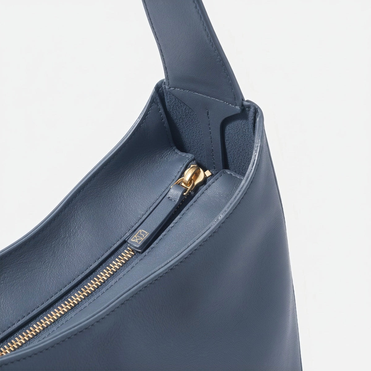 Blue handbag with gold zipper on a light gray background - Chambray