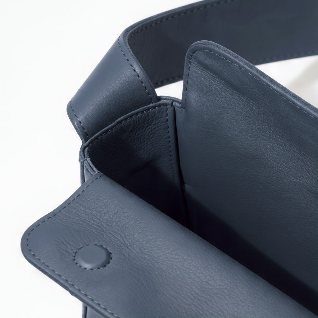 Close-up of a dark blue leather product with stitching details on a white background- Chambray