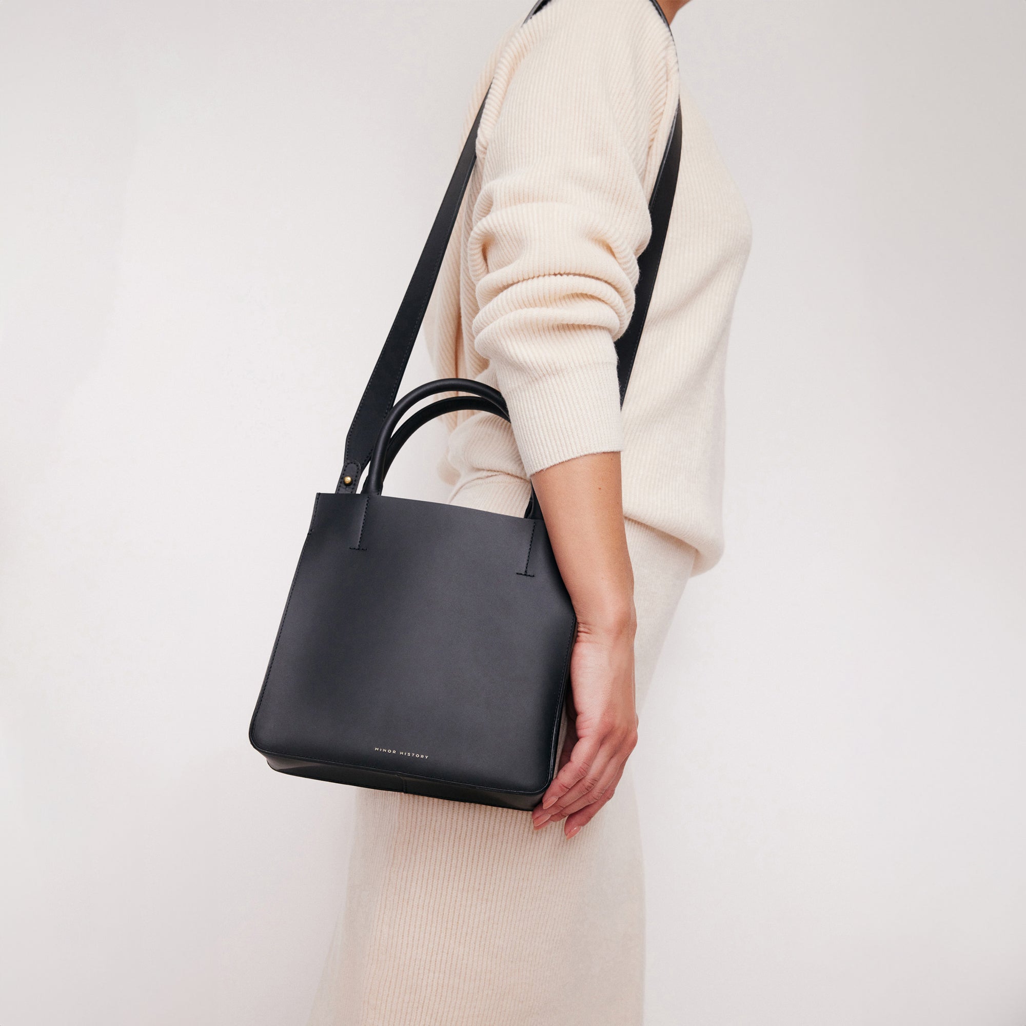 A silver crossbody leather bag with a removable strap and brass hardware, displayed against a plain background. - Sterling