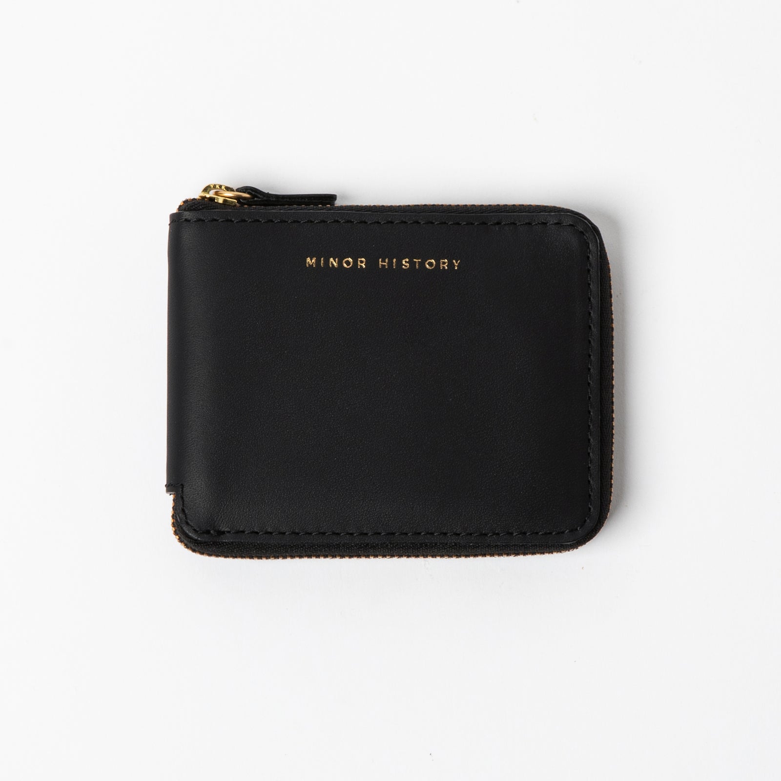 Brown wallet with 'Minor History' branding on a pink fabric background - Saddle