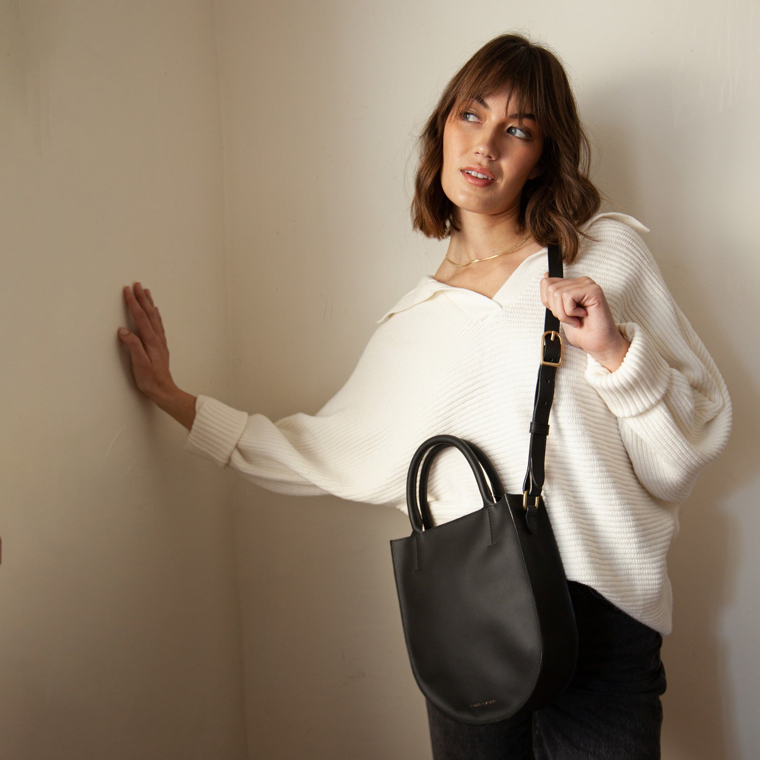 A black leather crossbody bag with an adjustable strap and solid brass hardware, viewed from the front. - Black